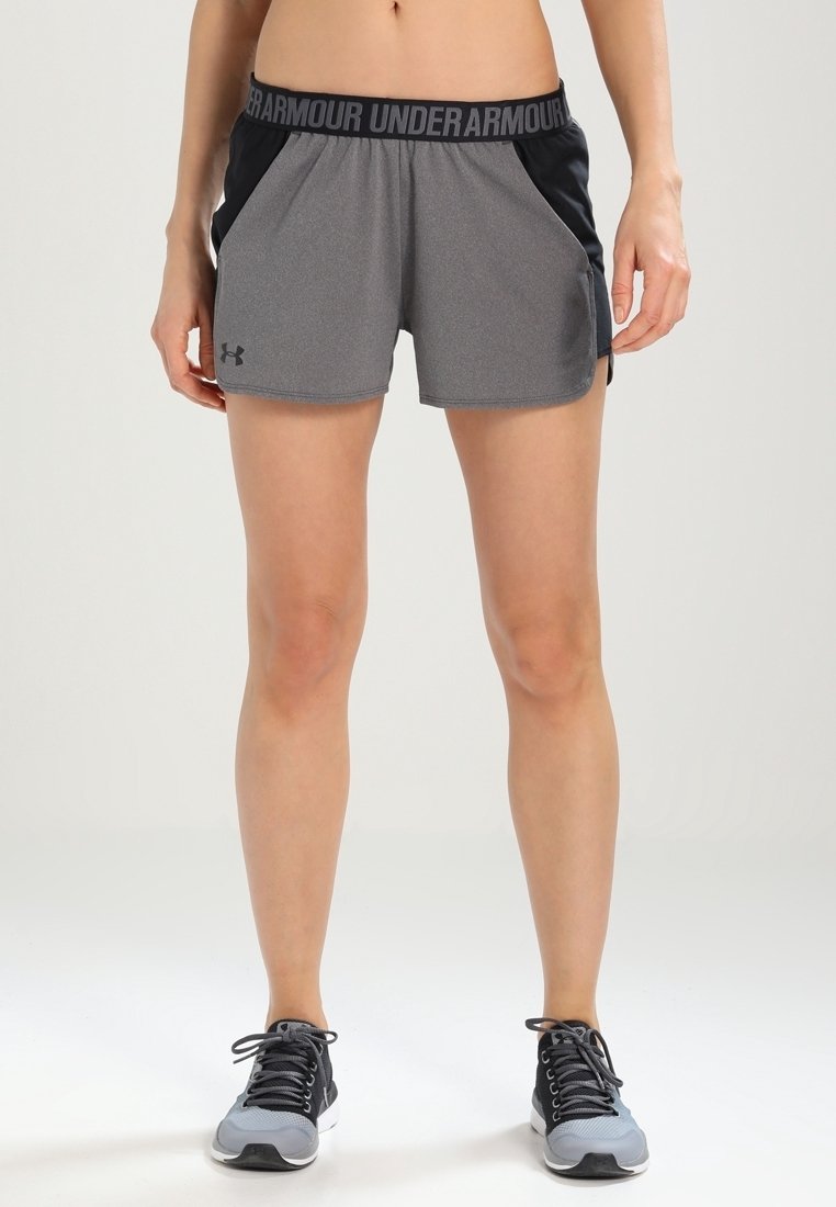 Grå sportshorts med svarta detaljer, tillverkade av fukttransporterande tyg. Har ett svart midjeband med texten "Under Armour".