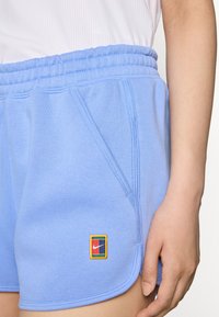 Šviesiai mėlyni sportiniai šortai su minkšta tekstūra, kurie turi šonines kišenes ir daugiaspalvę „Nike“ logotipo aplikaciją apatiniame kairiajame priekyje.