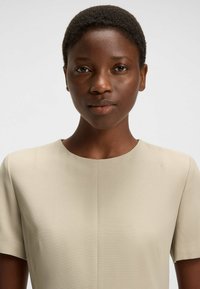 Beige kortärmad topp med rund halsringning och ett slätt, texturerat tyg. Har subtila sömmar och en minimalistisk design.