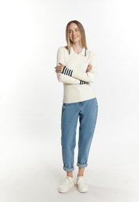 Ribbel, crèmekleurig langemouwtop met een polo kraag, voorzien van marineblauwe gestreepte boorden, in combinatie met opgerolde lichtblauwe jeans en witte sneakers.