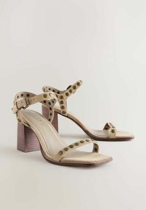 Beige suède hoge hak sandalen met grote ronde uitsparingen, verstelbare band en een stevige houten hak. Vierkante neusontwerp.