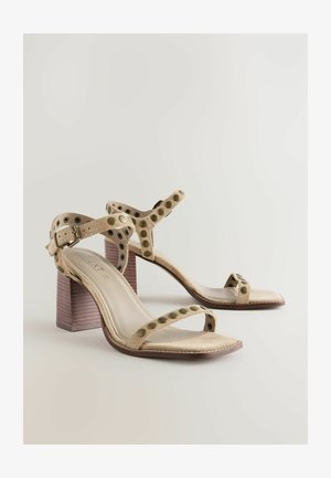 Beige suède hoge hak sandalen met grote ronde uitsparingen, verstelbare band en een stevige houten hak. Vierkante neusontwerp.