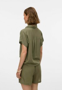 Camicia verde oliva a maniche corte abbinata a pantaloni corti coordinati. Tessuto leggero, vestibilità leggermente ampia e dettaglio a pieghe sul retro per il comfort.