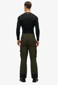 Zwarte longsleeve basislaag gecombineerd met olijfgroene cargobroek met zijzakken. De broek heeft een zwarte accentkleur aan de zoom.