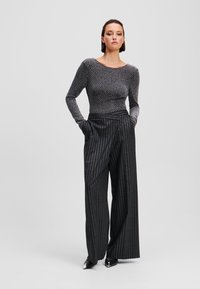 Zwart en zilver gestreepte wijde broek gecombineerd met een aansluitend langomfiguren top met een stippenpatroon, wat zorgt voor een slanke silhouet.