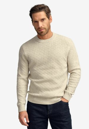 Suéter de punto beige con un patrón texturizado, cuello redondo y puños de canalé. Combinado con jeans de mezclilla oscura.