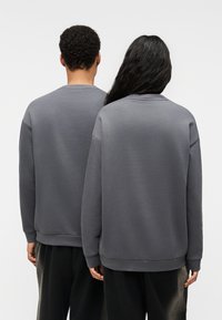Γκρι αποχρώσεις βαμβακερή φούτερ με λαιμόκοψη, χαλαρούς ώμους και ριμπ μανσέτες, που φοριέται από δύο φιγούρες από πίσω.