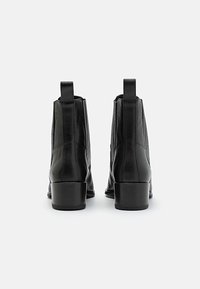 Svarta läderankelboots med en slät yta, rund tå, elastiska sidopaneler och en kort, blockklack. Har dragflikar bak.