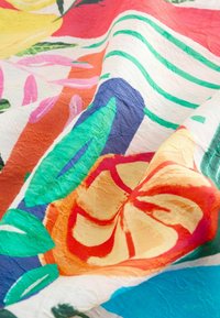 Tessuto decorato con colori vivaci come rosso, giallo e blu, con disegni floreali e strisce verdi, che mette in mostra una superficie texture.