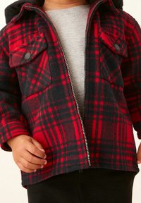 Röd och svart rutigt fleecejacka med dragkedja och stora framsidans fickor. Har en huva och ribbade ärmslut. Slät grå innervaddering.