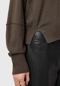 Maglione marrone a maglia con polsini a coste, caratterizzato da spacchi ai lati, abbinato a pantaloni in pelle nera, con texture liscia e forma aderente.