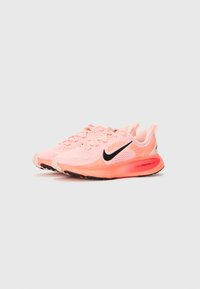 Nike running shoes in bright pink mesh, featuring a black swoosh, textured patterns, and a cushioned orange outsole with grip details.