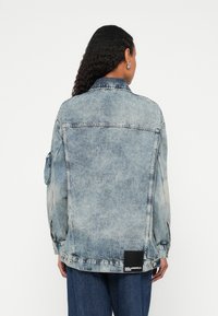 Jeans jakna v svetlo modri barvi, z žepom na rami, logotipno oznako na robu in standardnim ovratnikom. Enostaven in udoben kroj.