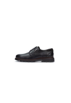 Zapato de vestir de cuero negro con acabado suave, punta redonda y costuras decorativas. Presenta una suela de goma y un diseño de cordones con un pequeño acento.