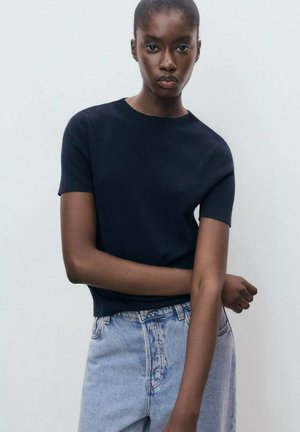 Marineblauwe korte mouwen gebreide top gecombineerd met lichtblauwe high-waisted jeans, met een ronde halslijn en een getailleerde pasvorm.
