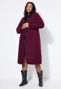 Cappotto in lana bordeaux con vestibilità rilassata, maniche lunghe, ampio colletto e chiusura a bottoni, abbinato a stivali cowboy neri.