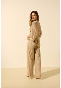 Une tenue en or scintillant avec un haut drapé et plissé et un pantalon large, présentant un éclat métallique texturé et une coupe décontractée.