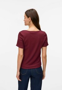 Camisa de manga corta en burdeos con un acabado texturizado y un escote barco, combinada con jeans de color azul oscuro. Presenta un diseño ajustado y un estilo informal.