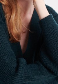 Tmavě zelený pletený svetr s hlubokým výstřihem do V a oversized rukávy, s texturovaným vzorem a měkkým, útulným vzhledem.