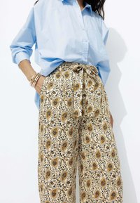 Chemise bleu clair à manches longues assortie à un pantalon crème ample présentant un motif paisley et floral complexe en jaune et bleu.