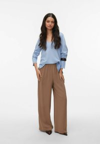 Haut à manches longues bleu clair avec un décolleté en V, associé à un pantalon large marron. La tenue se caractérise par des textures douces et une coupe décontractée.