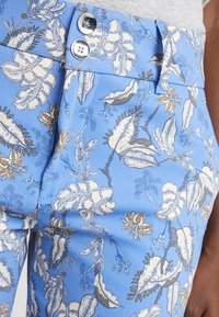 Blue patterned trousers featuring floral designs in white and gold accents. Includes a two-button closure and textured fabric.