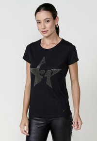 Zwarte katoenen t-shirt met een metalen rhinestone sterontwerp aan de voorkant. Getailleerde vorm met korte mouwen en een ronde hals.