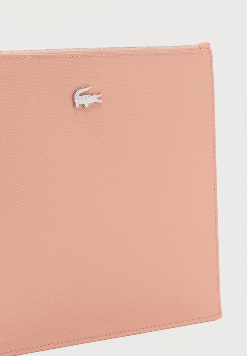 Zachte roze textuur zakje met een klein wit krokodillenlogo in het midden bovenaan, met gestikte randen en een ritssluiting bovenaan.