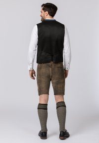 Schwarze Weste, weißes Hemd, braune Lederhosen, knielange gemusterte Socken in Grau und schwarze Schuhe. Einfaches Design mit minimalen Verzierungen.