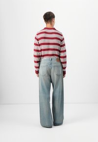 Pull rayé bordeaux et blanc avec des poignets côtelés associé à un jean en denim bleu clair à jambes larges, doté de poches arrière et d'une patch en cuir.