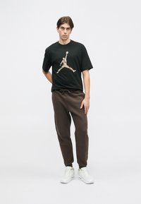 Czarna koszulka z grafiką koszykarza, w zestawie z brązowymi dresami i białymi sneakerami, o luźnym kroju i zapinanej na sznurek talii.