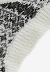 Tissu de pull tricoté couleur crème avec un motif géométrique noir. Texture douce, légèrement duveteuse avec des bords côtelés pour le contraste.