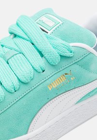 Zapatilla de ante verde menta con cordones trenzados, acentos blancos y una suela de goma texturizada. Presenta la marca dorada "PUMA Suede XL".