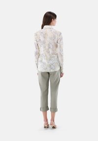 Camicia a maniche lunghe con motivo floreale chiaro, in tessuto morbido; abbinata a pantaloni verdi chiari arrotolati e scarpe con tacco beige, vista da dietro.