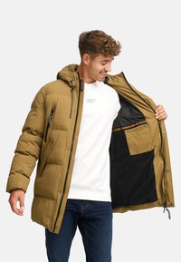 Quilted parka i olivengrøn med hætte, har lynlåslommer og en kontrasterende sort foring. Indeni er der en lomme til opbevaring.
