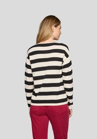 Gestreifter Pullover in Schwarz und Creme mit lockerer Passform, geripptem Textur und überschnittenen Schultern, kombiniert mit roten Hosen.