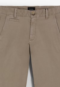 Pantalones de algodón beige con corte recto, con cierre de botón, bolsillos frontales y detalles de costura sutiles. Etiqueta de la marca visible.
