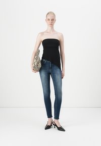 Black strapless top, blue skinny jeans, and black pointed heels. Holding a textured, beige snake-patterned bag. Sits against a white background.
