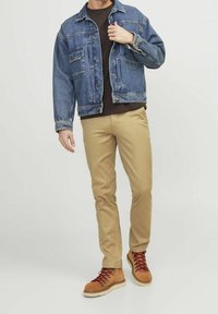 Giacca di jeans blu sopra una maglia scura, pantaloni beige e stivali marroni con lacci rossi. La giacca presenta tasche e una vestibilità comoda.
