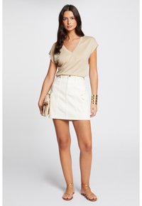 Lichtbeige V-hals top met korte mouwen, gecombineerd met een witte denim rok met frontzakken en een gouden knoopsluiting.