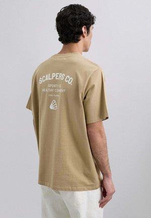 Camiseta de algodón color arena con mangas cortas. Presenta texto y logo en blanco en la parte de atrás. Textura suave, corte relajado. Diseño simple y versátil.