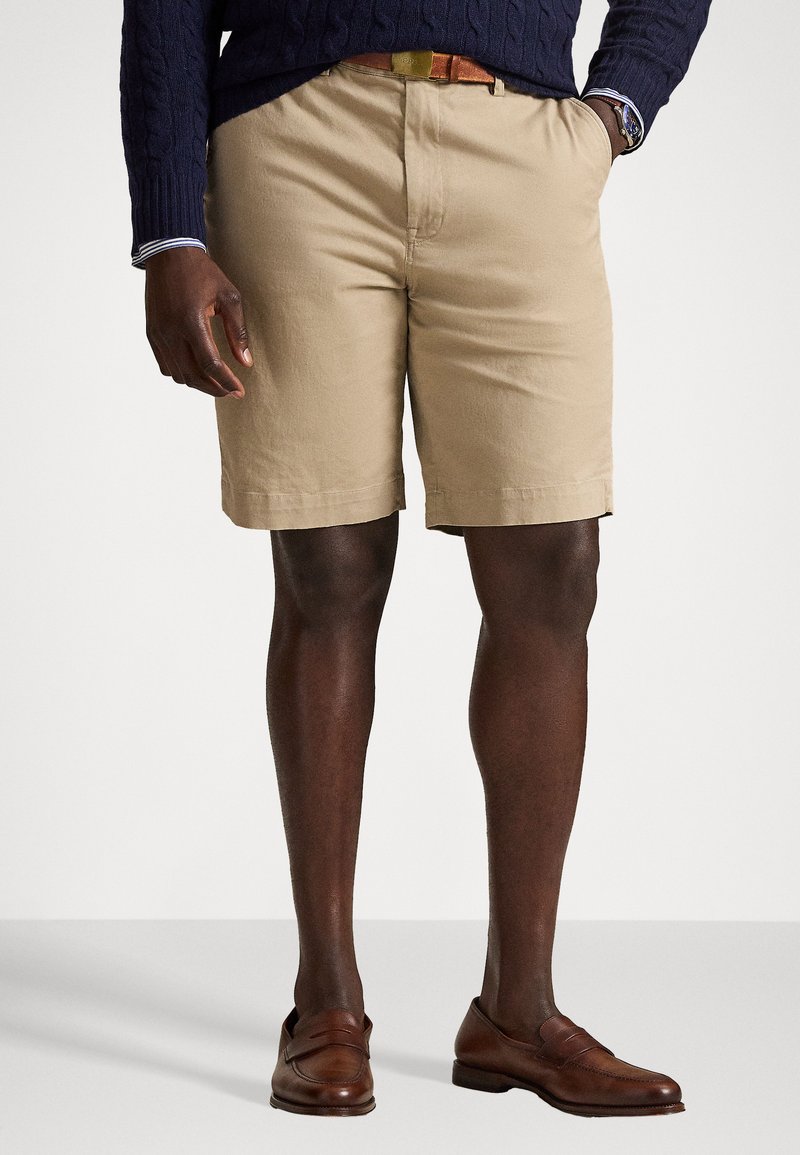 Μπεζ βαμβακερές βερμούδες με ίσιο μπροστινό μέρος, θηλύκια για ζώνη και πλαϊνές τσέπες, συνδυασμένες με καφέ δερμάτινα μοκασίνια.