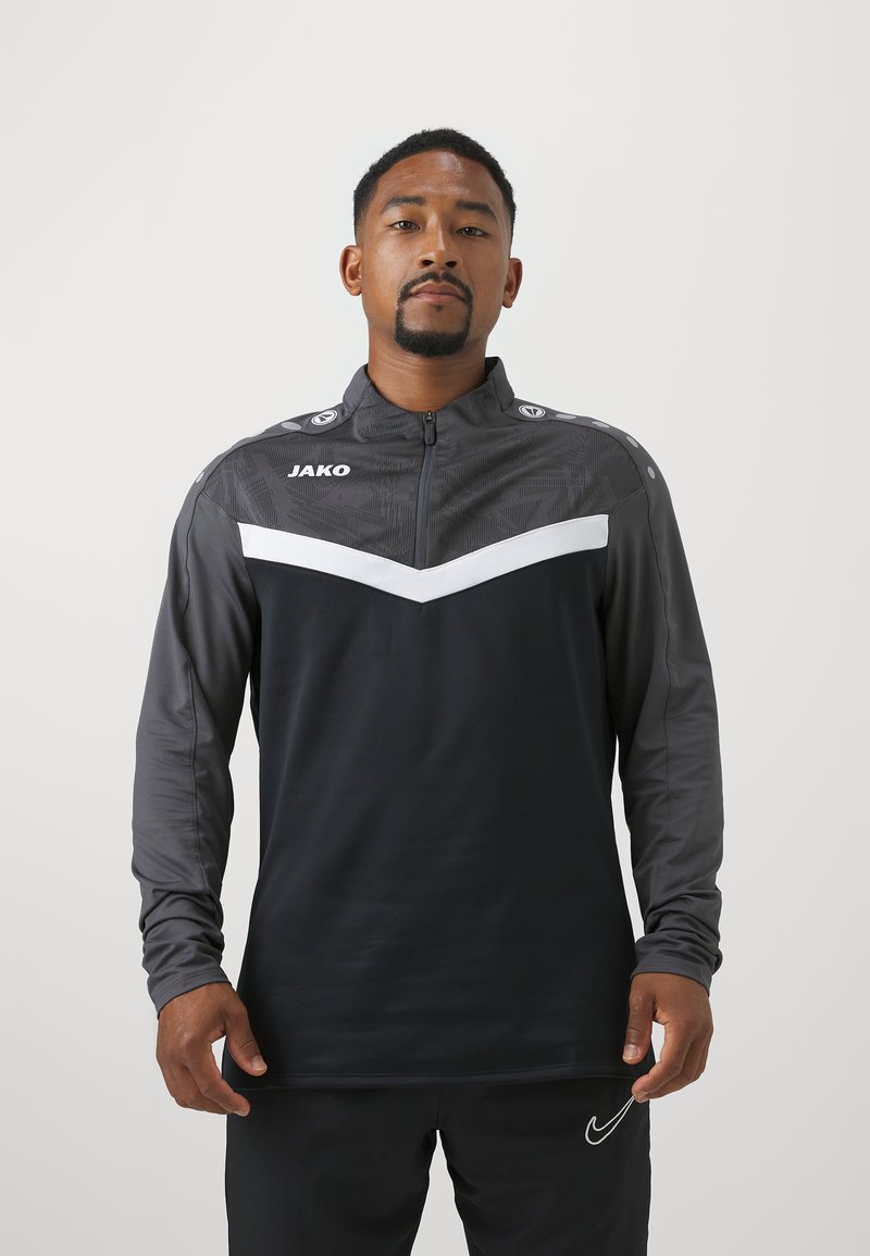 Schwarze und graue sportliche Zip-Jacke mit einem weißen Chevron-Muster, langen Ärmeln und Logo-Akzenten an den Schultern. Glatte Stoffstruktur.