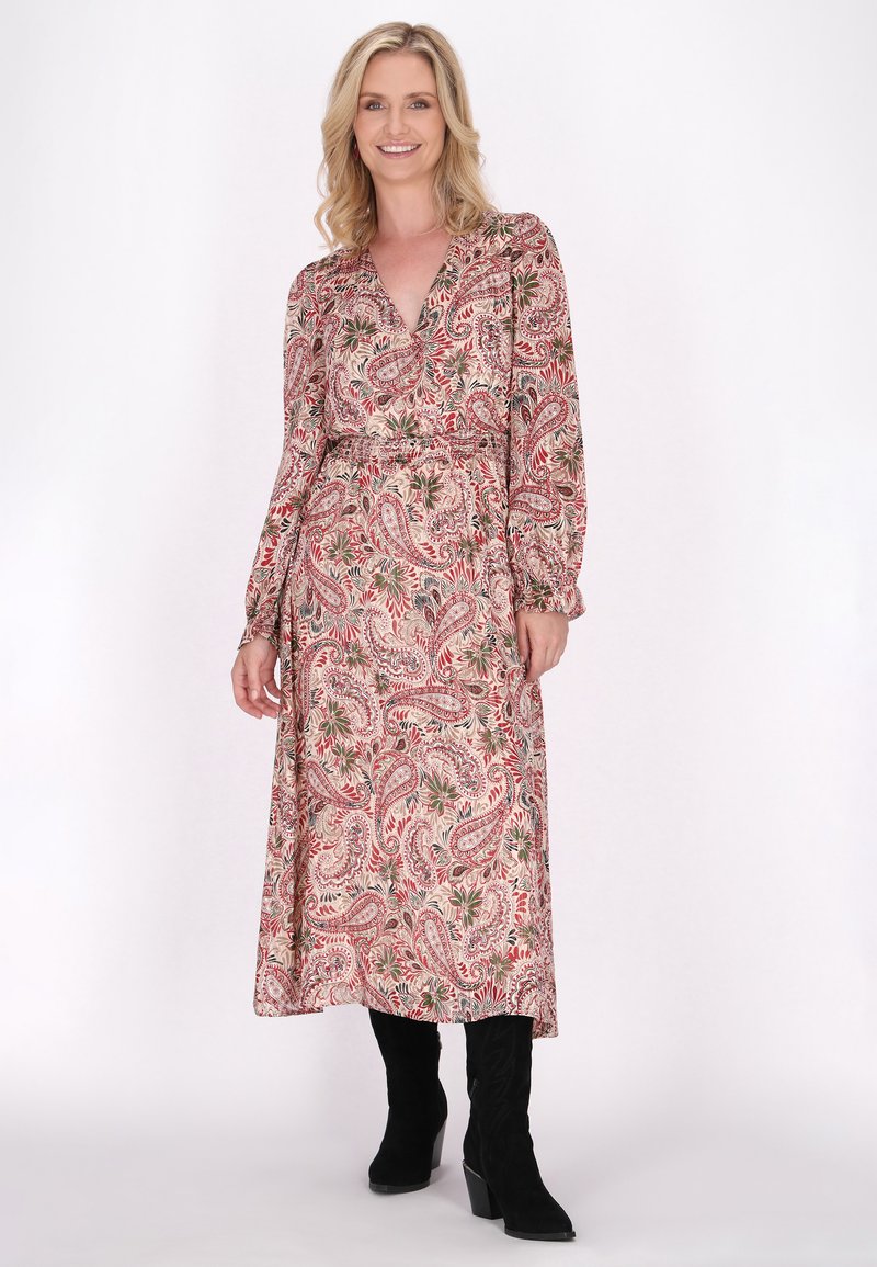Rochie lungă, cu imprimeu floral paisley în nuanțe de roșu, verde și crem, cu mâneci lungi și decolteu în v, asortată cu cizme negre până la genunchi.