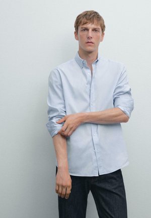 Lichtblauw overhemd van katoen met lange mouwen, voorzien van een kraag en opgerolde manchet, gecombineerd met donkere denim jeans.