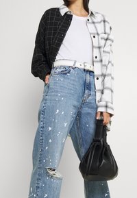 Camicia a quadri oversized bianco e nero, t-shirt bianca, jeans chiari strappati con macchie di vernice e borsa a secchiello in pelle nera.