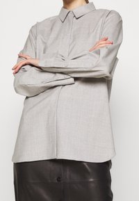 Hellgrau button-up Hemd mit langen Ärmeln und einem Kragen. Verfügt über einen strukturierten Stoff und einen abgerundeten Saum, kombiniert mit einem schwarzen Lederrock.