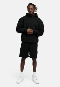 Black hoodie with large neckline and long sleeves paired with black drawstring shorts. Worn with white sneakers and socks.