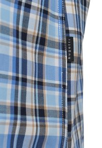 Blaue Karostoff mit verschiedenen Blautönen, Braun und Weiß. Enthält ein sichtbares Markenlabel, das in die Seitennaht genäht ist.