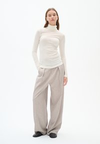 Light beige turtleneck top in a smooth fabric, paired with gray wide-leg trousers with pleats. Model stands on a white background.